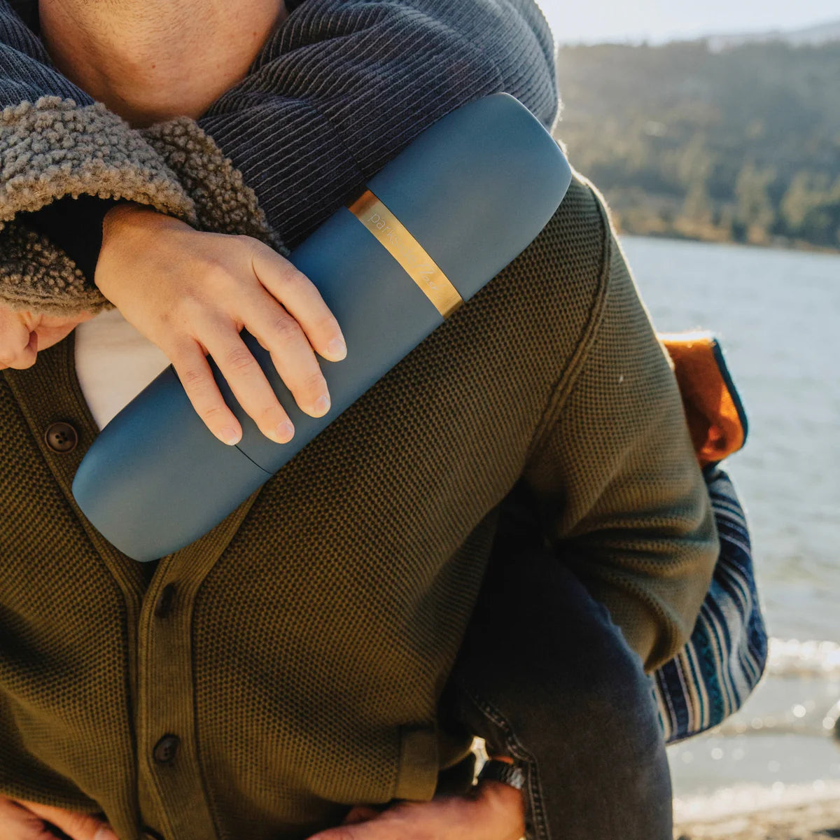 Person holding a blue and gold container by a lake