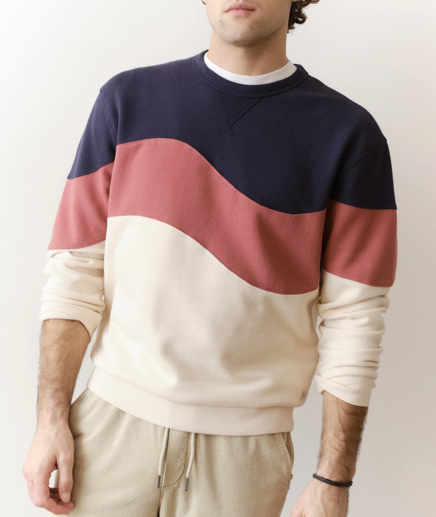 Person wearing a color-blocked sweater with navy, red, and beige sections on a plain background.