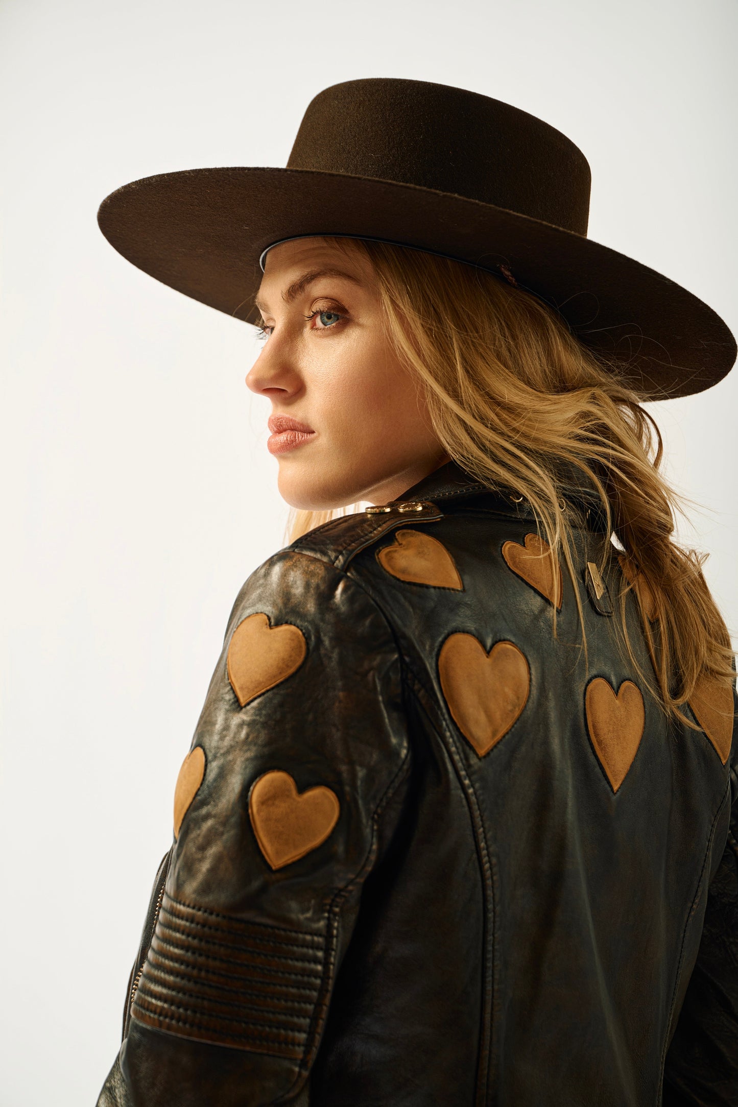Woman wearing a brown leather jacket with heart patterns and a matching hat on a white background