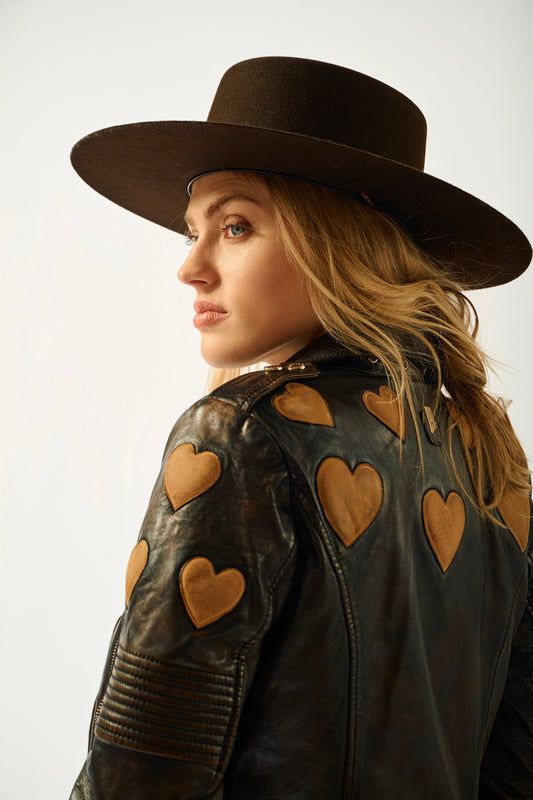 Woman wearing a brown leather jacket with heart patterns and a matching hat on a white background