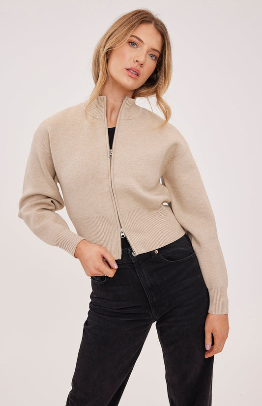 Woman wearing a beige zip-up cardigan against a white background