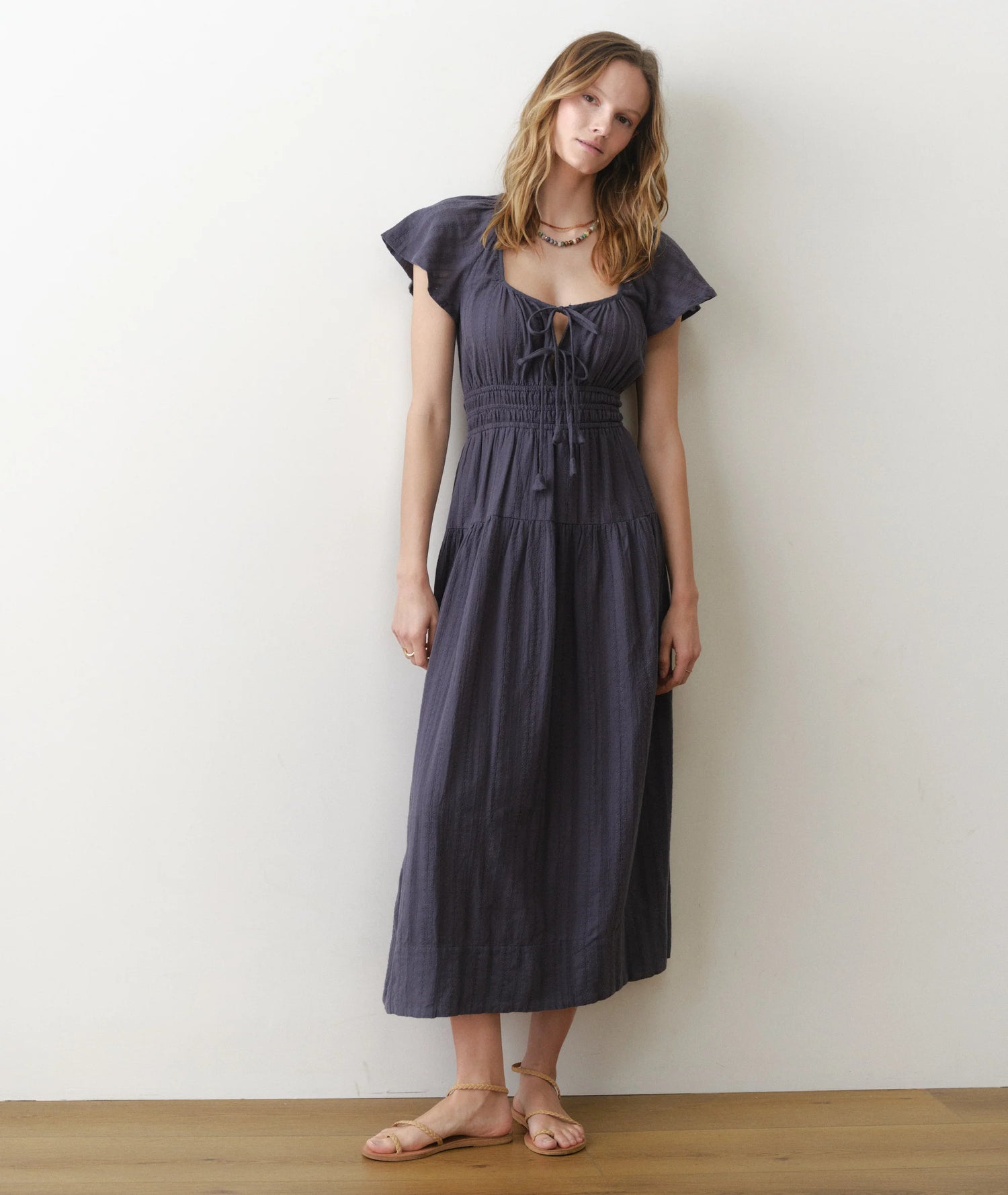 Woman wearing a dark blue dress against a white wall.