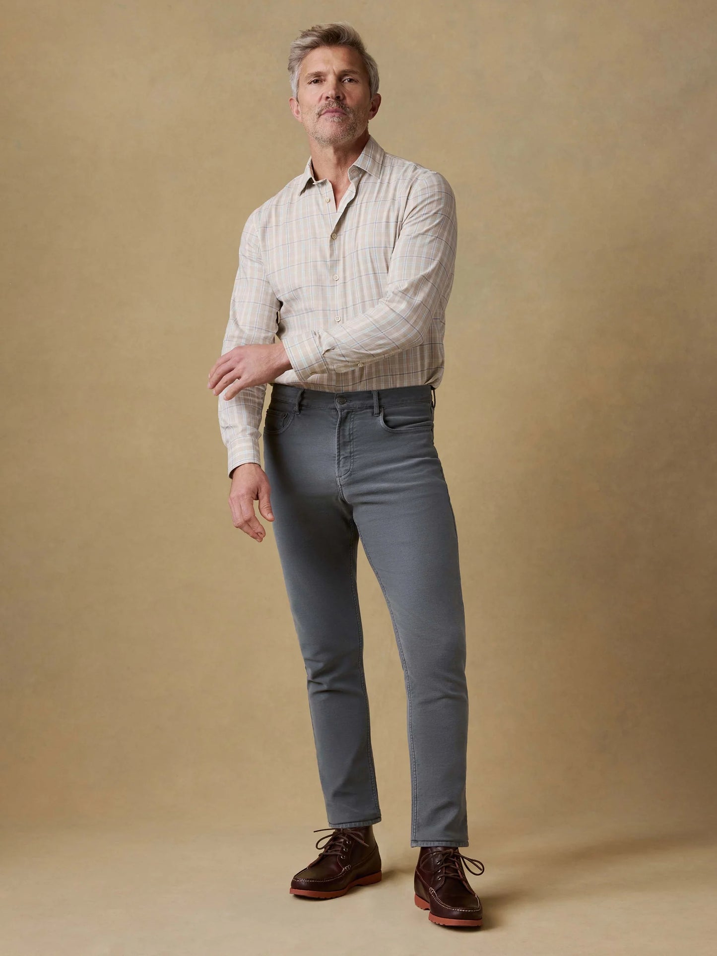 Man wearing a light-colored shirt, gray pants, and brown shoes against a beige background