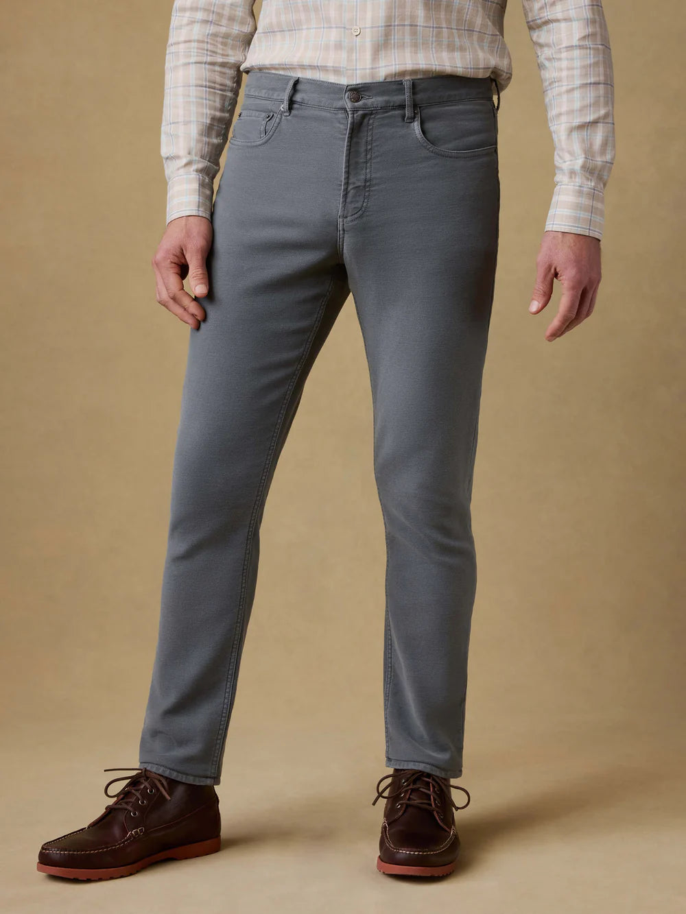 Person wearing gray pants and a plaid shirt on a beige background