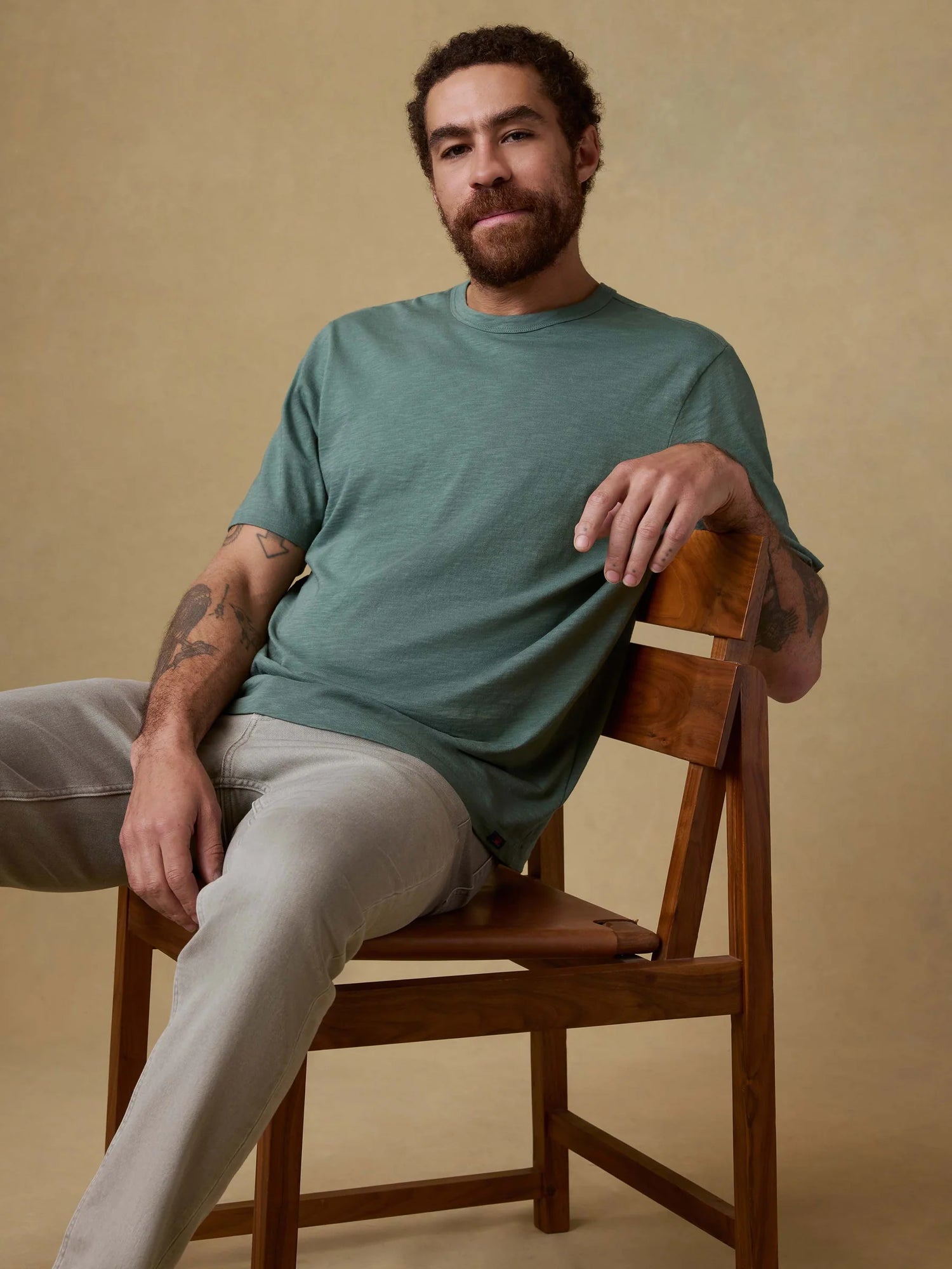 Man sitting on a wooden chair wearing a green t-shirt against a beige background