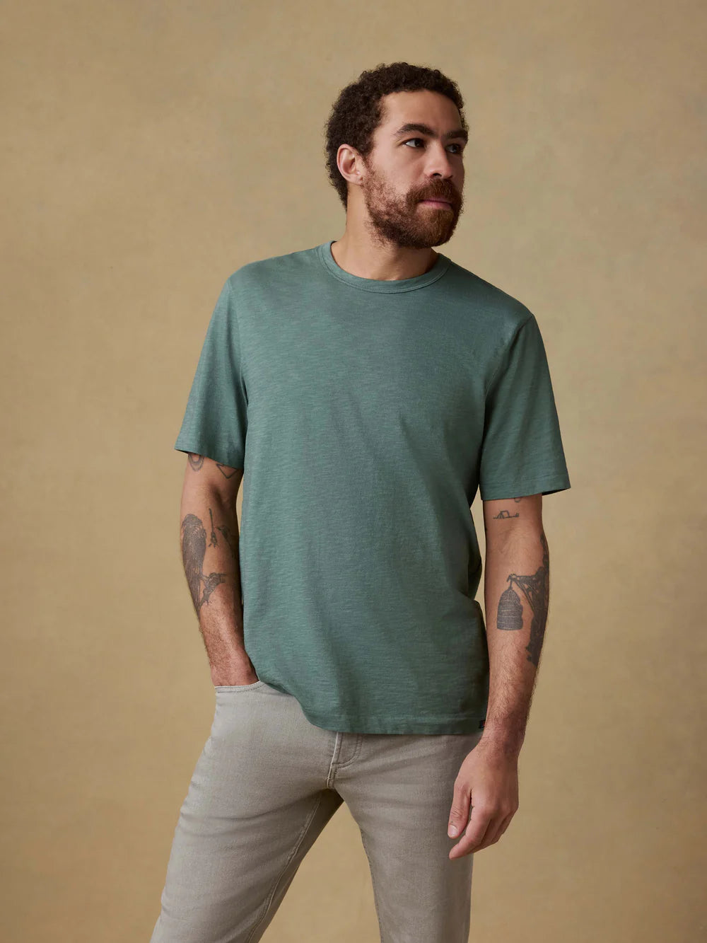 Man wearing a green t-shirt and beige pants against a beige background
