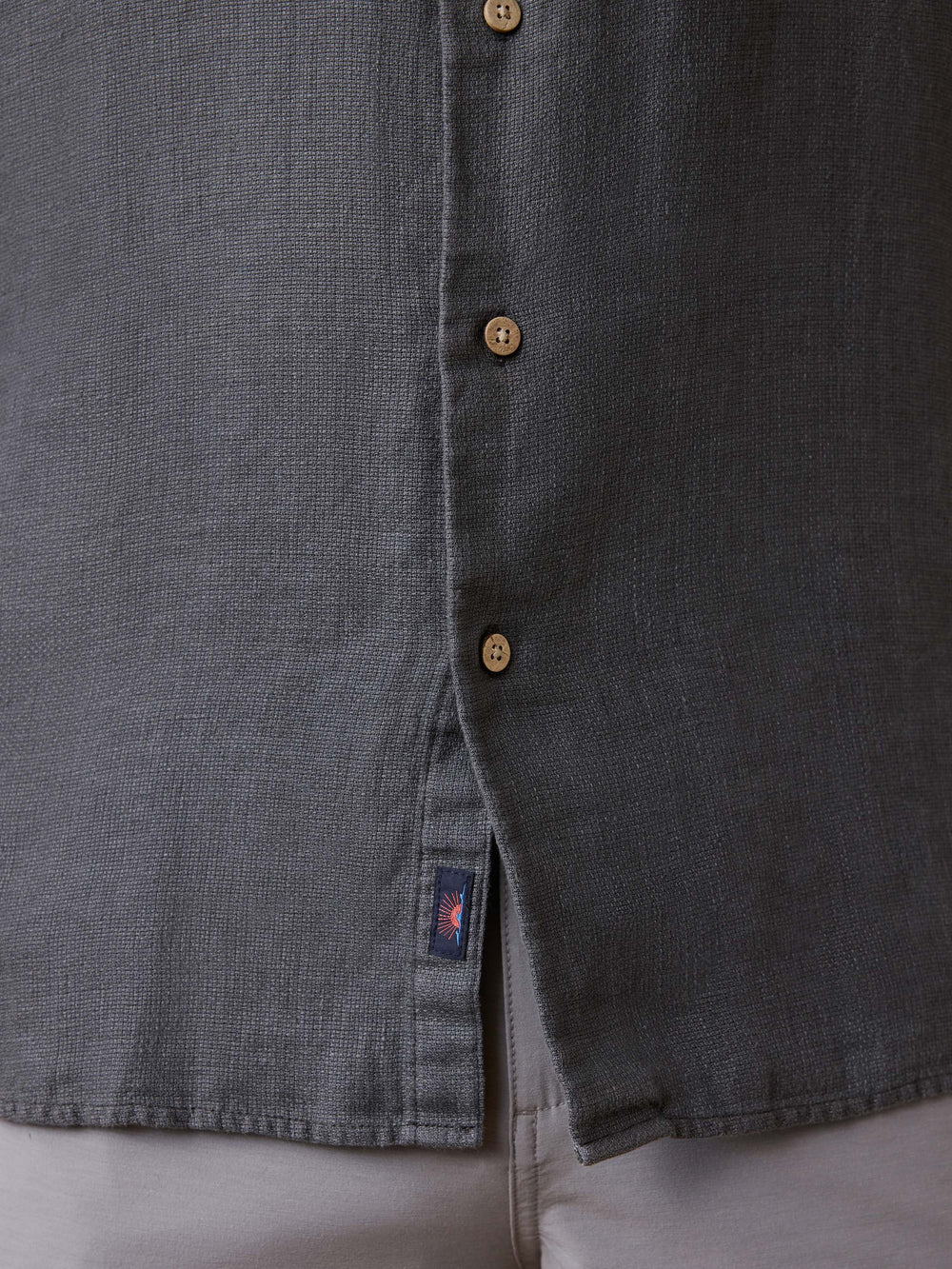 Close-up of a dark gray button-up shirt with a brand label on a light gray background