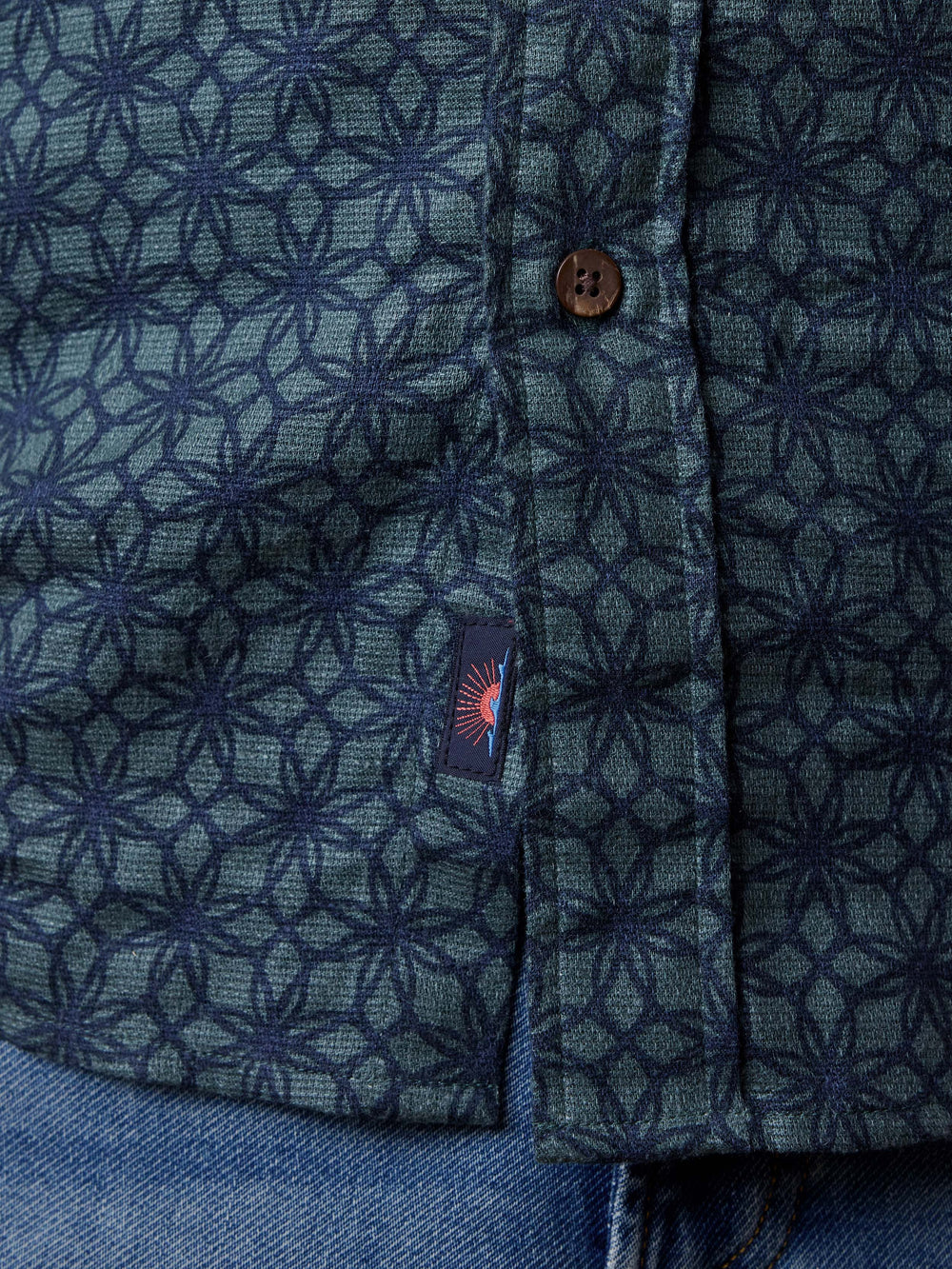 Close-up of a blue patterned shirt with a brand logo on a blue background