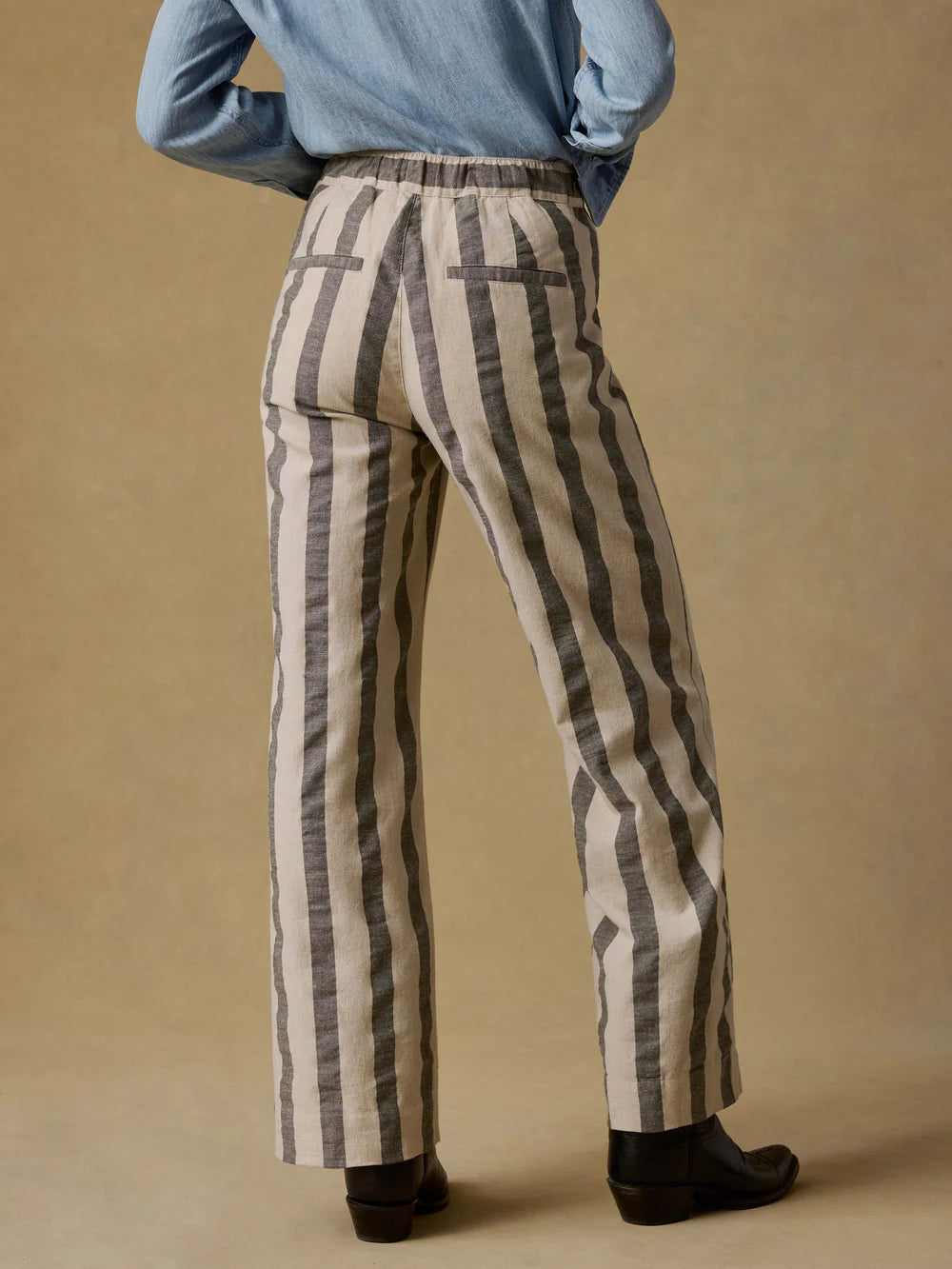 Person wearing striped pants and a blue sweater on a beige background