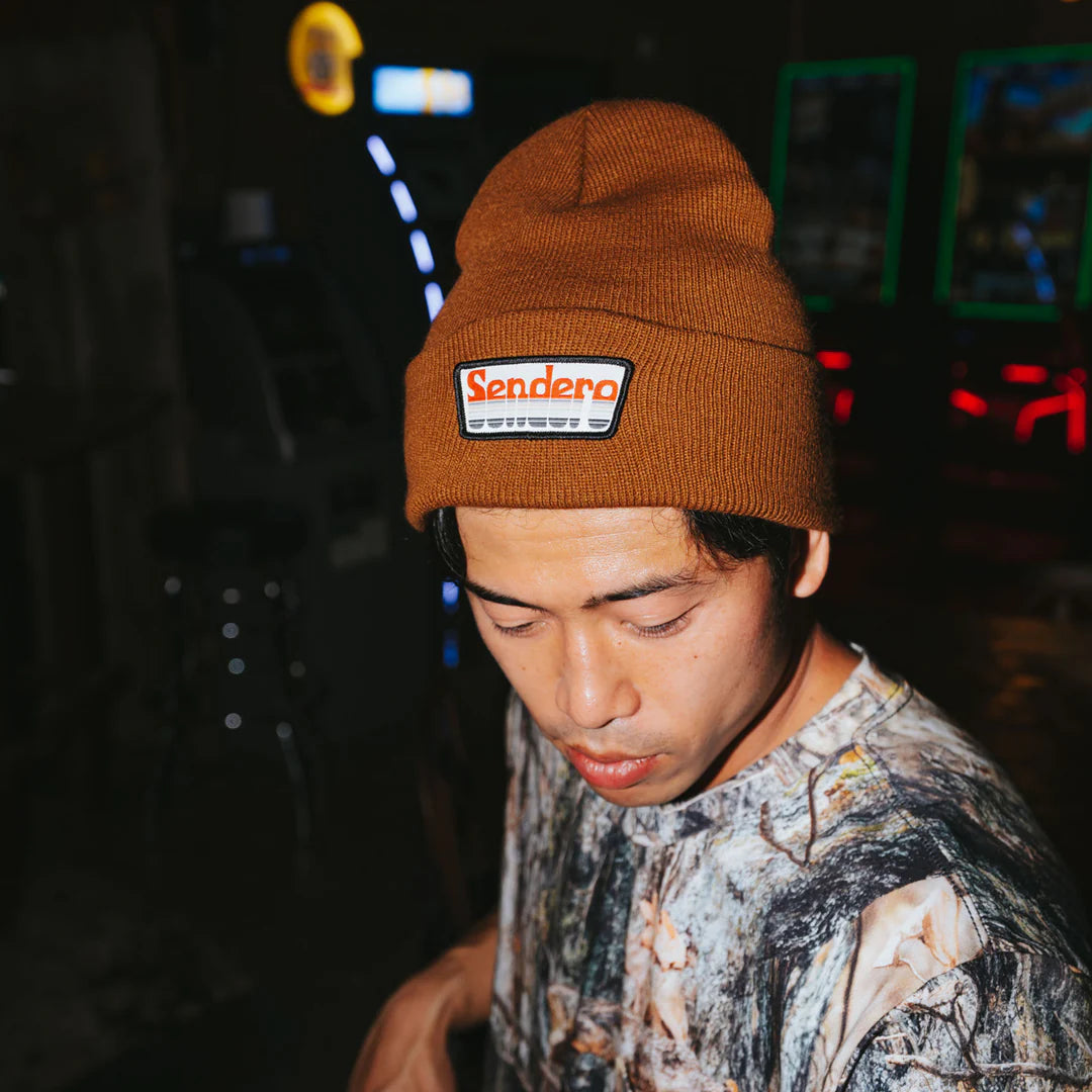 Person wearing a brown beanie with 'Sendero' logo at night.