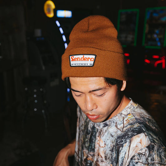 Person wearing a brown beanie with 'Sendero' logo at night.