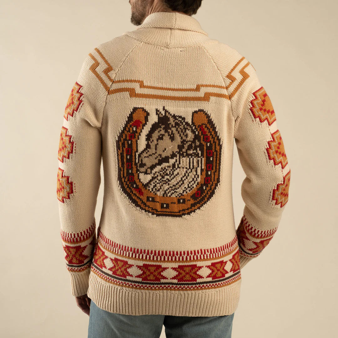 Person wearing a cream-colored sweater with a horse and horseshoe design on the back, against a beige background.