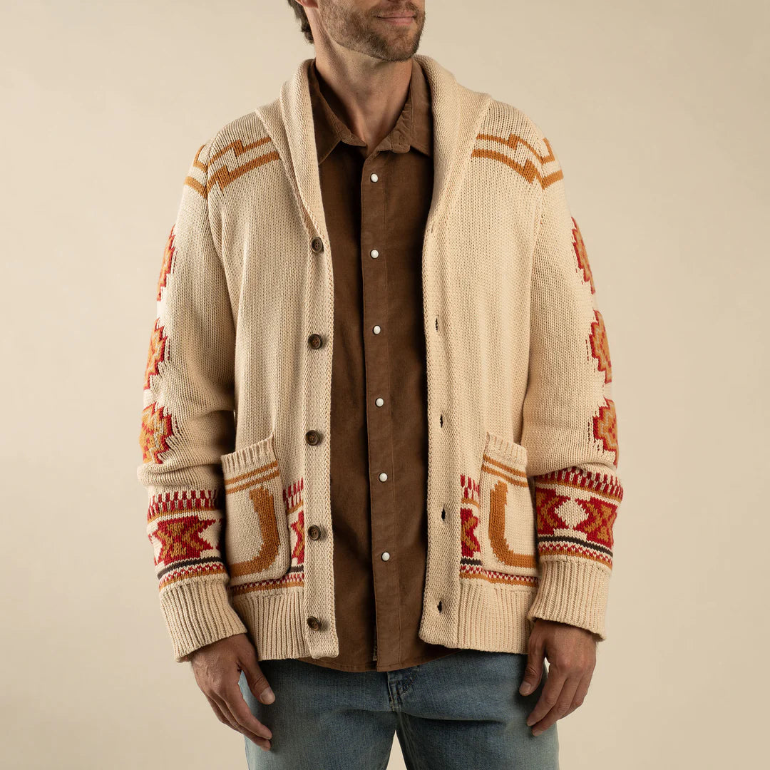 Man wearing a beige cardigan with red and orange patterns over a brown shirt on a beige background