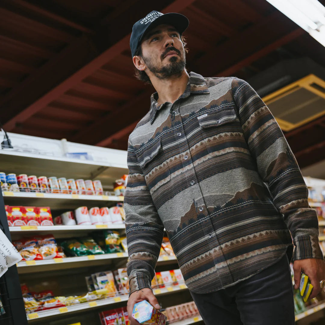 Man in a striped shirt and cap standing in a grocery store aisle.