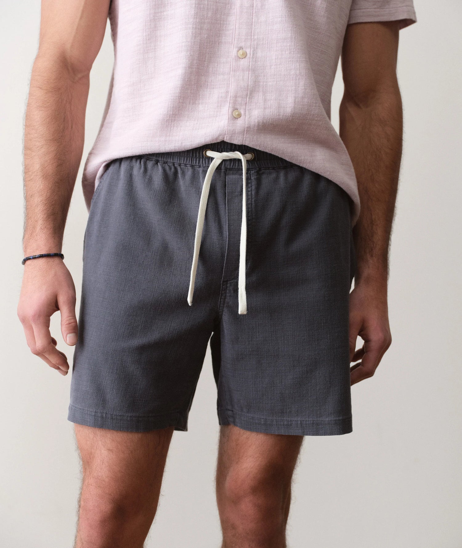 Person wearing dark shorts with a white drawstring on a plain background