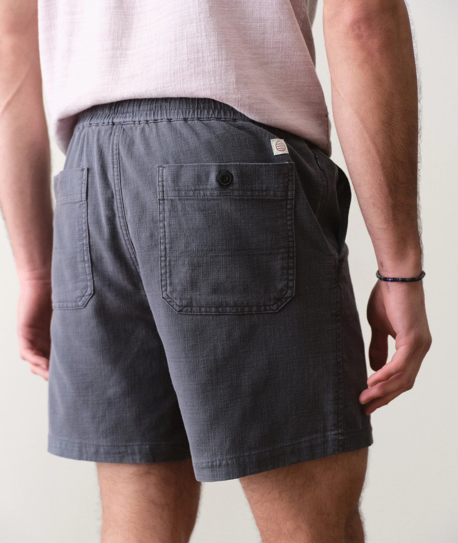 Person wearing dark gray shorts with a visible brand logo on a plain background