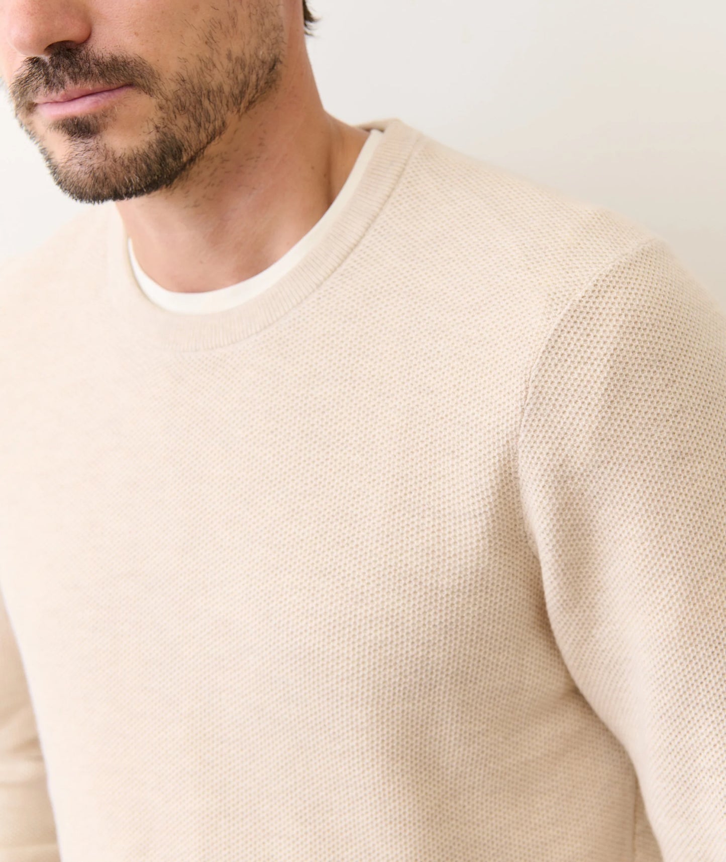 Close-up of a person wearing a beige sweater against a white background
