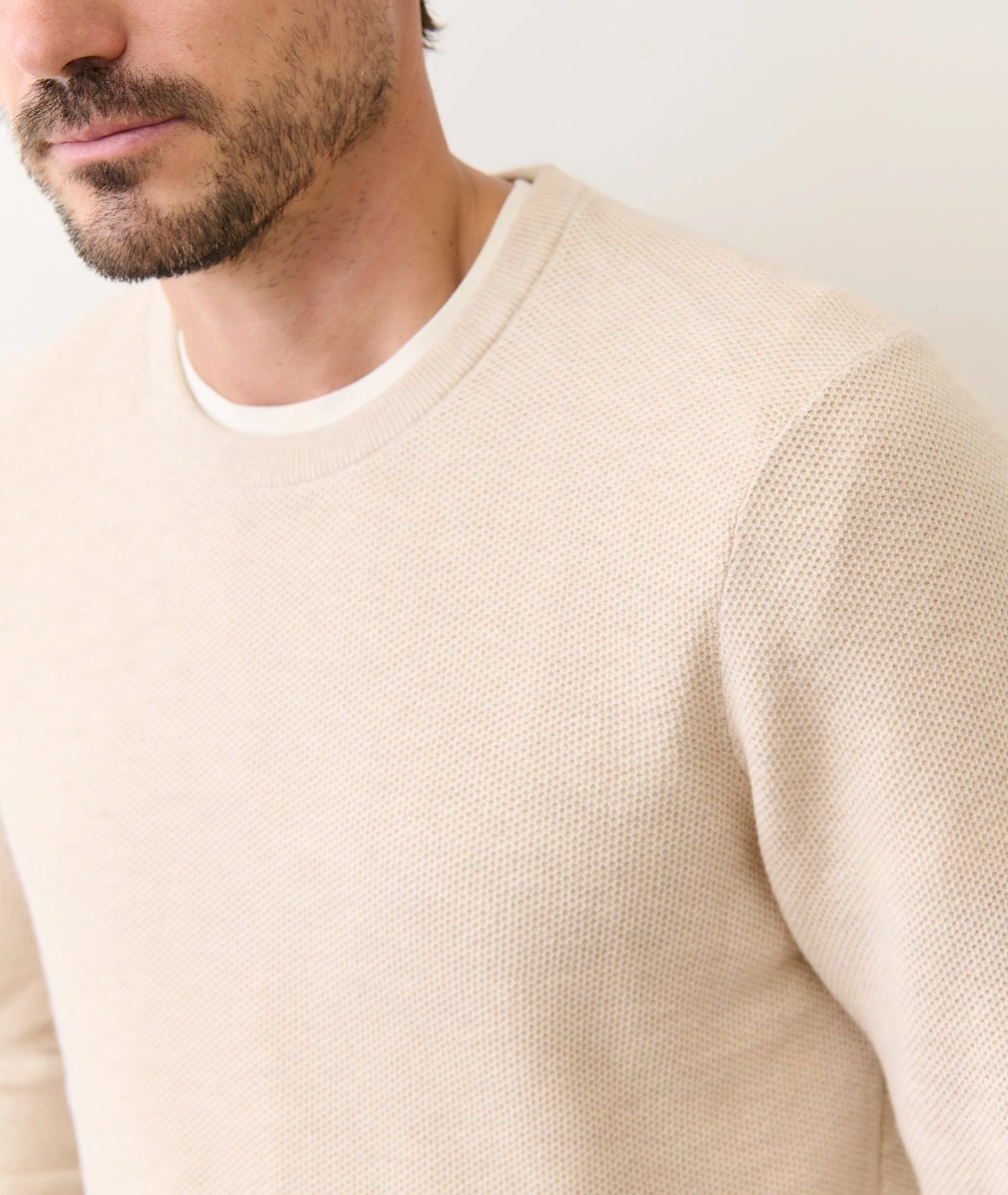 Close-up of a person wearing a beige sweater against a white background