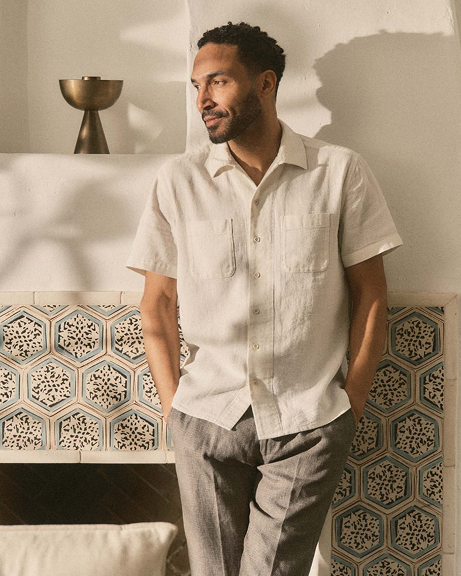 Man wearing a light-colored shirt and gray pants standing in a room with decorative tiles.