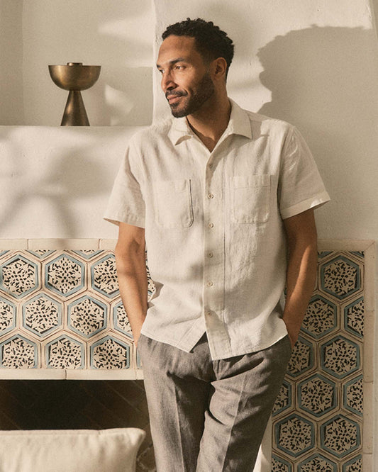 Man wearing a light-colored shirt and gray pants standing in a room with decorative tiles.