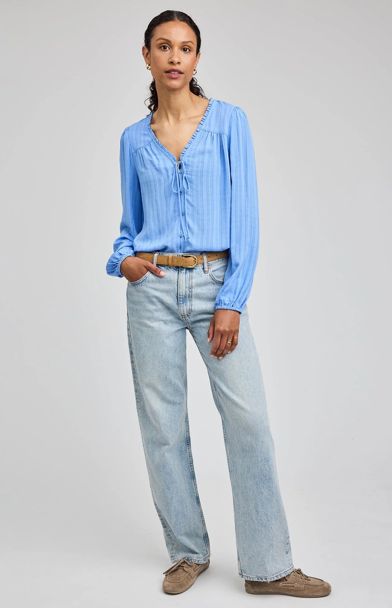 Woman wearing a light blue shirt and light blue jeans on a gray background