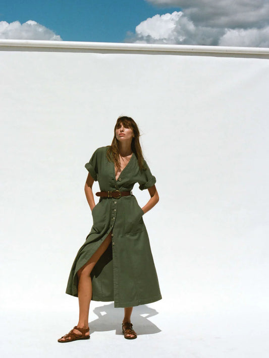 Woman in a green dress standing against a white wall with blue sky and clouds.