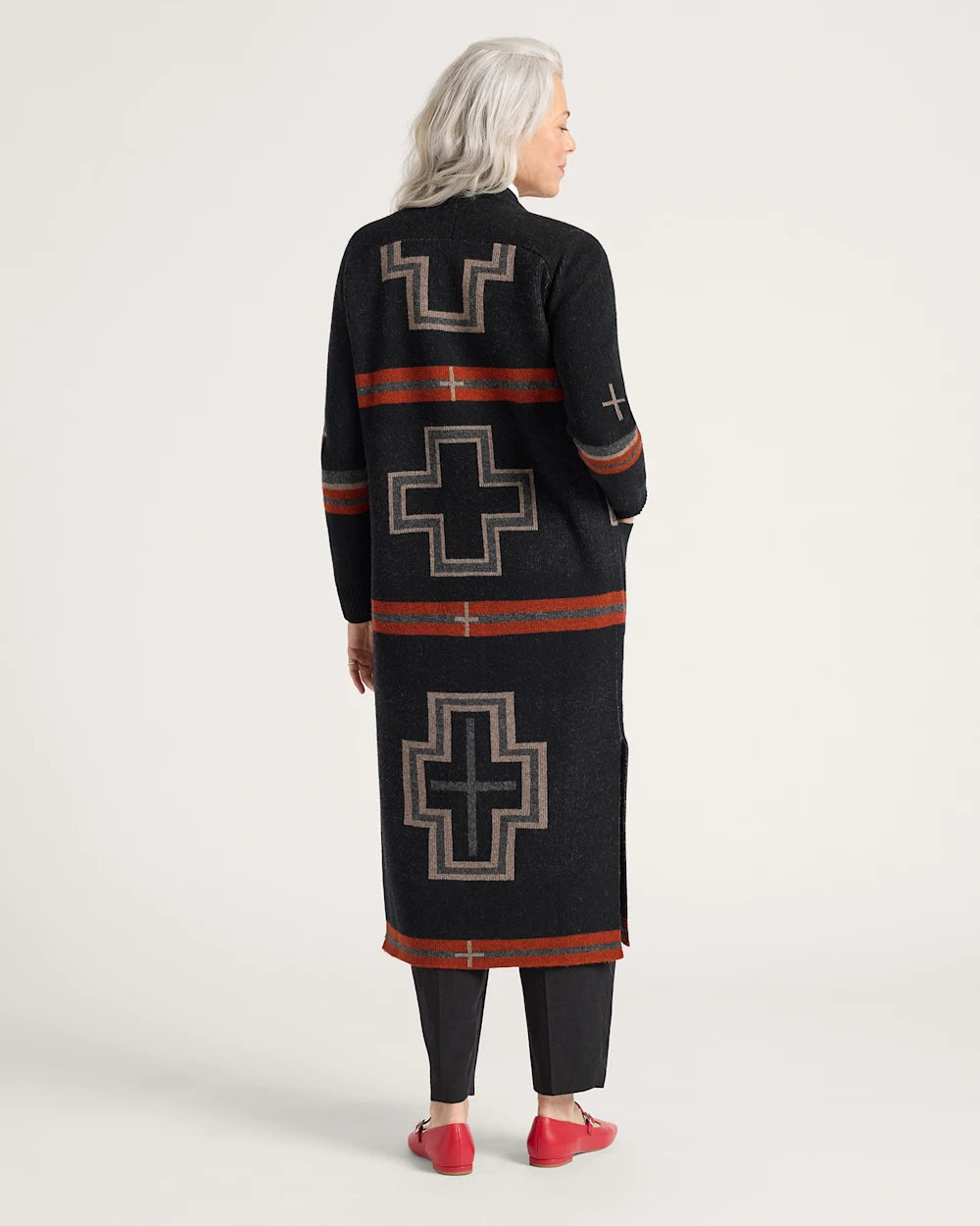 Person wearing a long black cardigan with geometric patterns on a white background