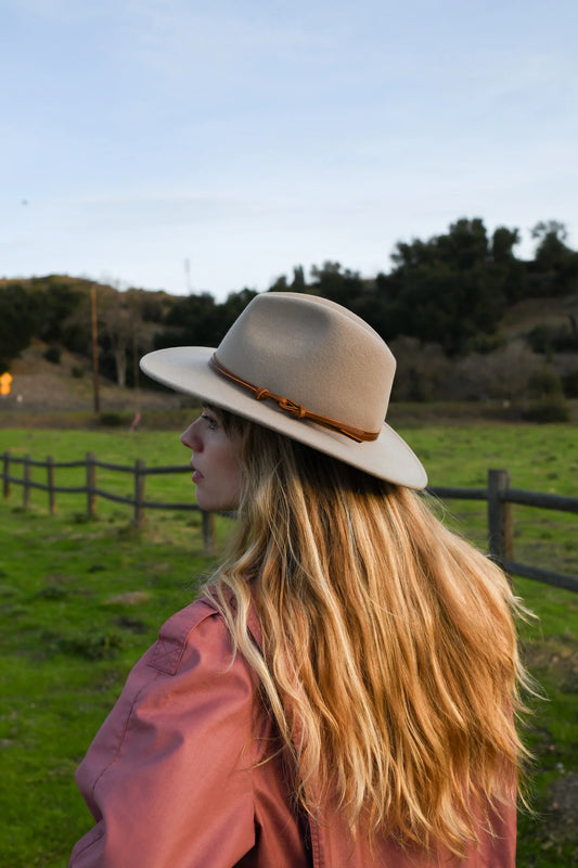 Woman wearing a beige hat in a field with a wooden fence and trees in the background