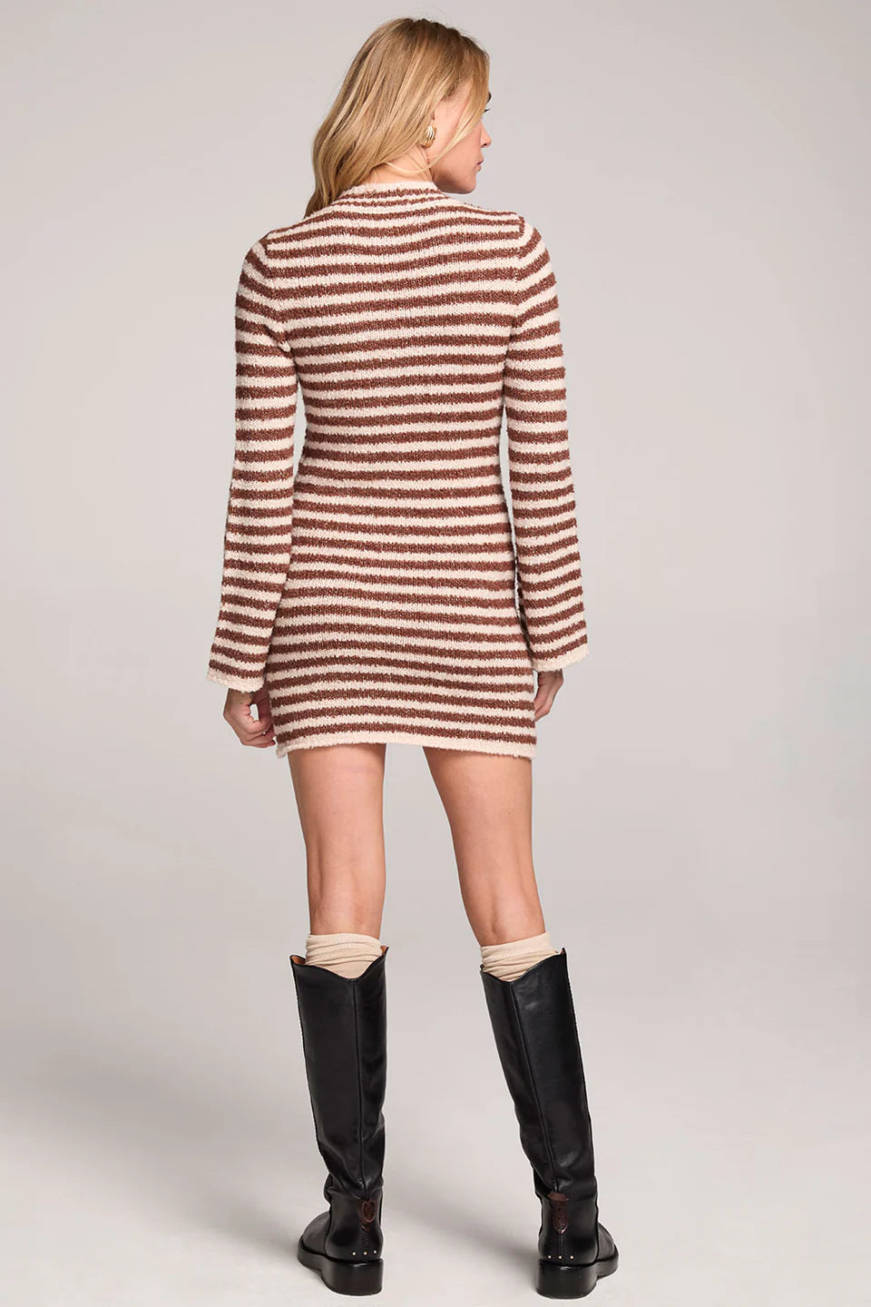 Person wearing a striped dress and black knee-high boots on a plain background