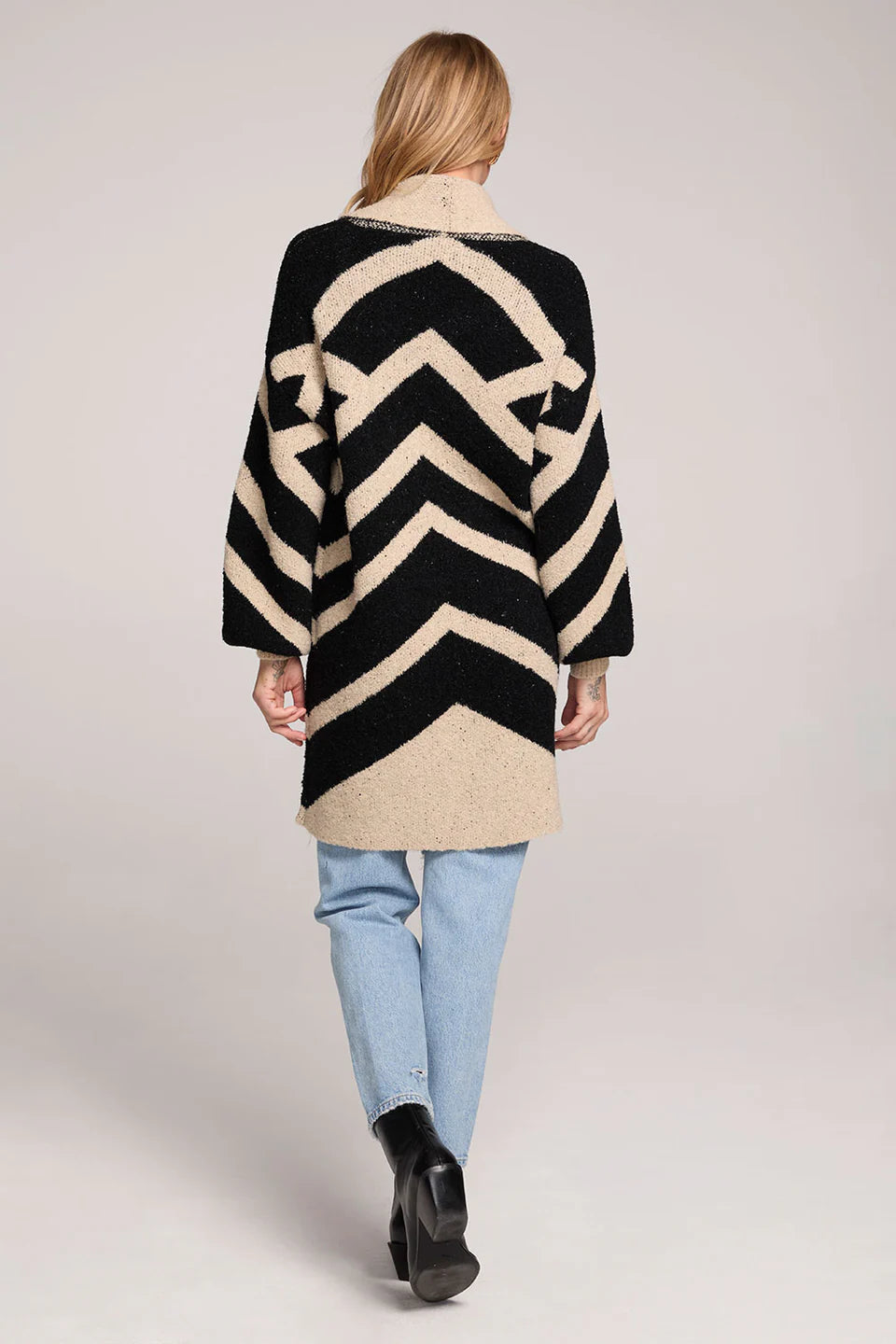 Person wearing a black and beige chevron patterned sweater on a plain background