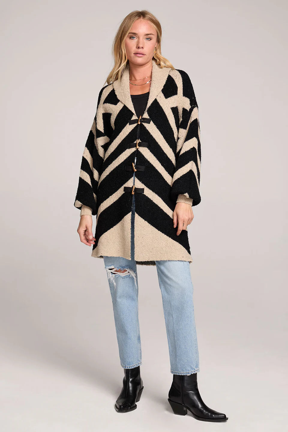 Woman wearing a black and beige patterned coat with light blue jeans on a plain background