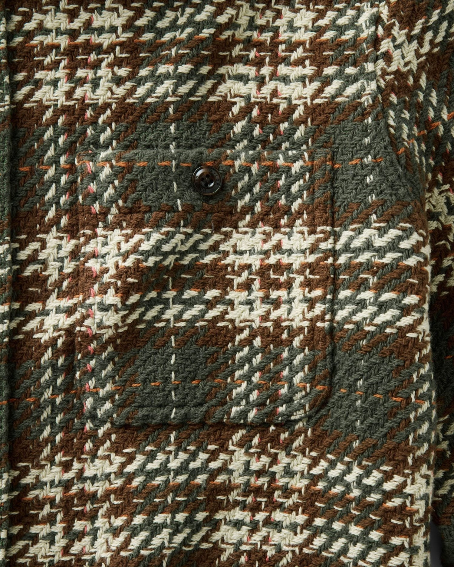 Close-up of a textured woven fabric with a brown, cream, and gray houndstooth pattern, featuring a buttoned pocket.