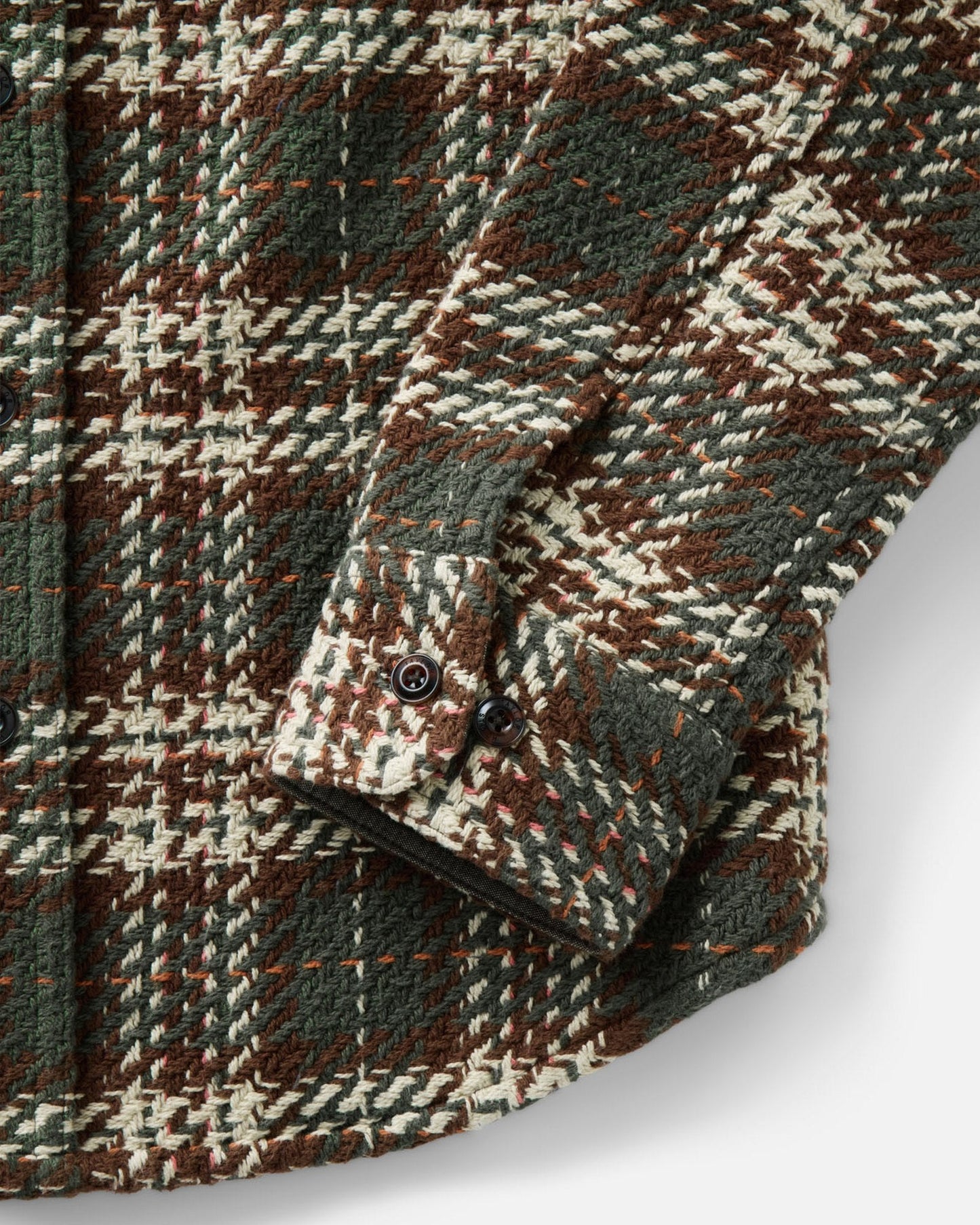 Close-up of a textured plaid wool shirt jacket in brown, green, and cream, showing the fabric weave and buttoned cuff.