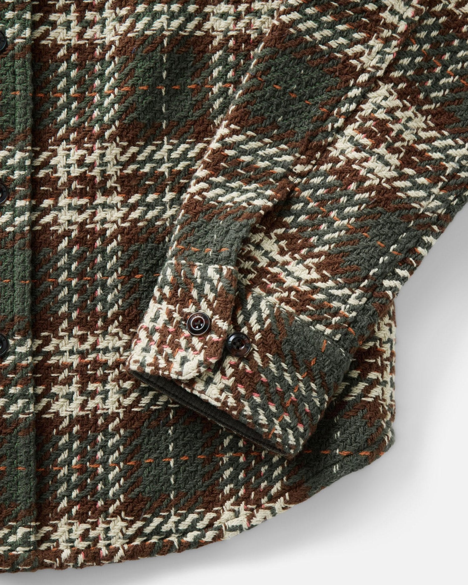 Close-up of a textured plaid wool shirt jacket in brown, green, and cream, showing the fabric weave and buttoned cuff.