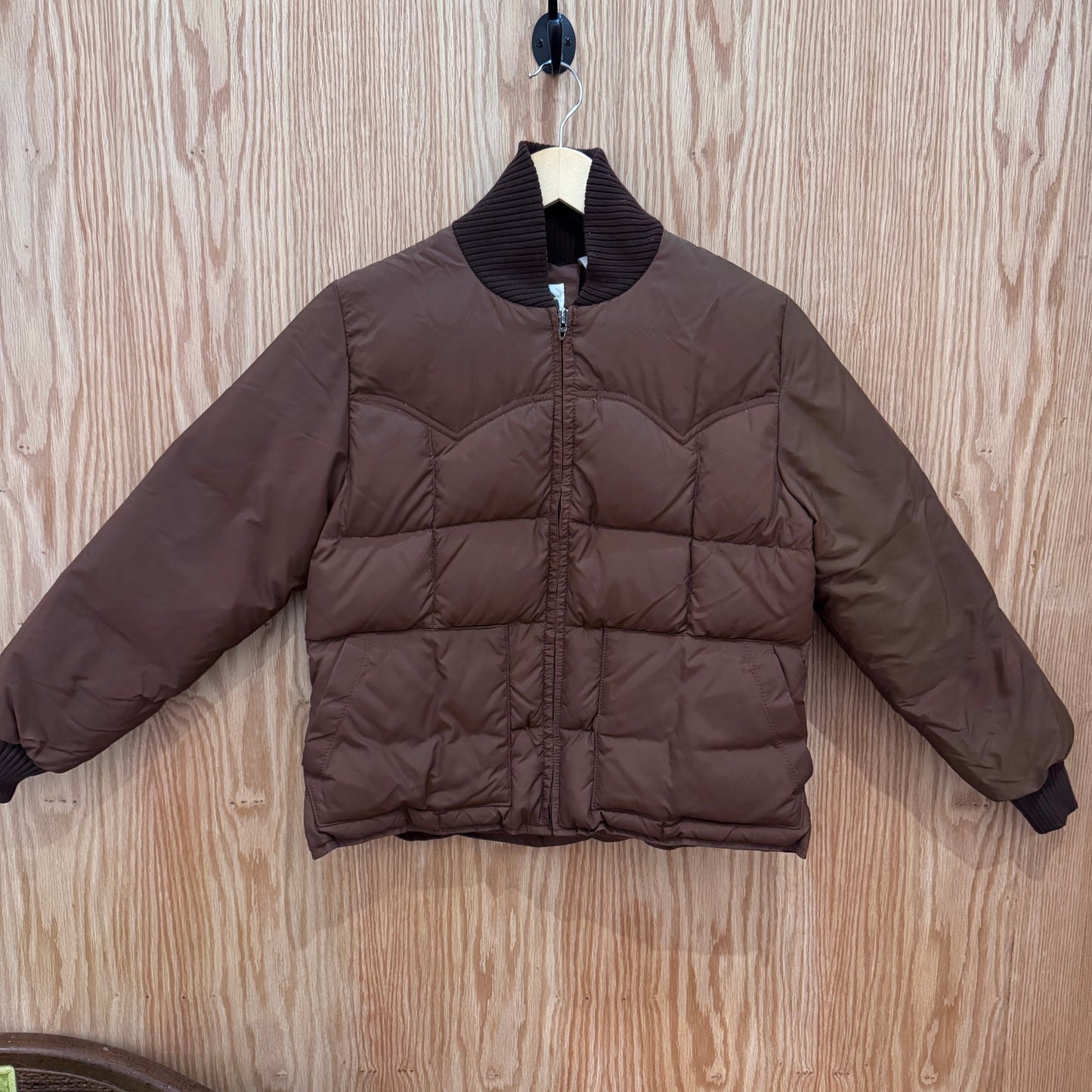 Brown puffer jacket on a hanger against a wooden background