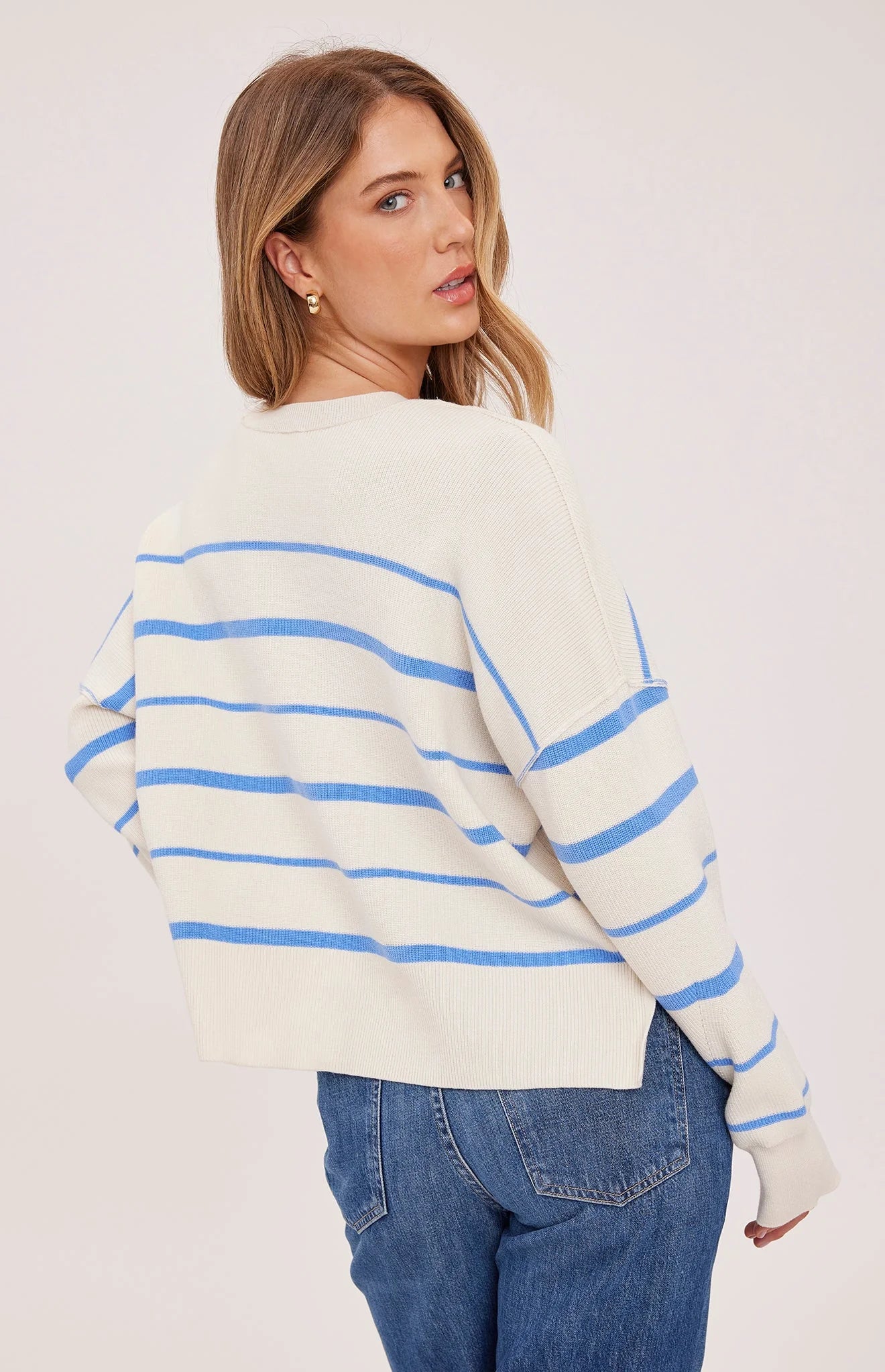 Woman wearing a cream sweater with blue stripes and blue jeans on a white background