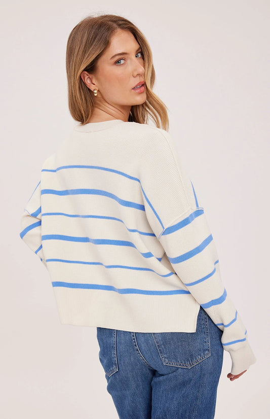 Woman wearing a cream sweater with blue stripes and blue jeans on a white background
