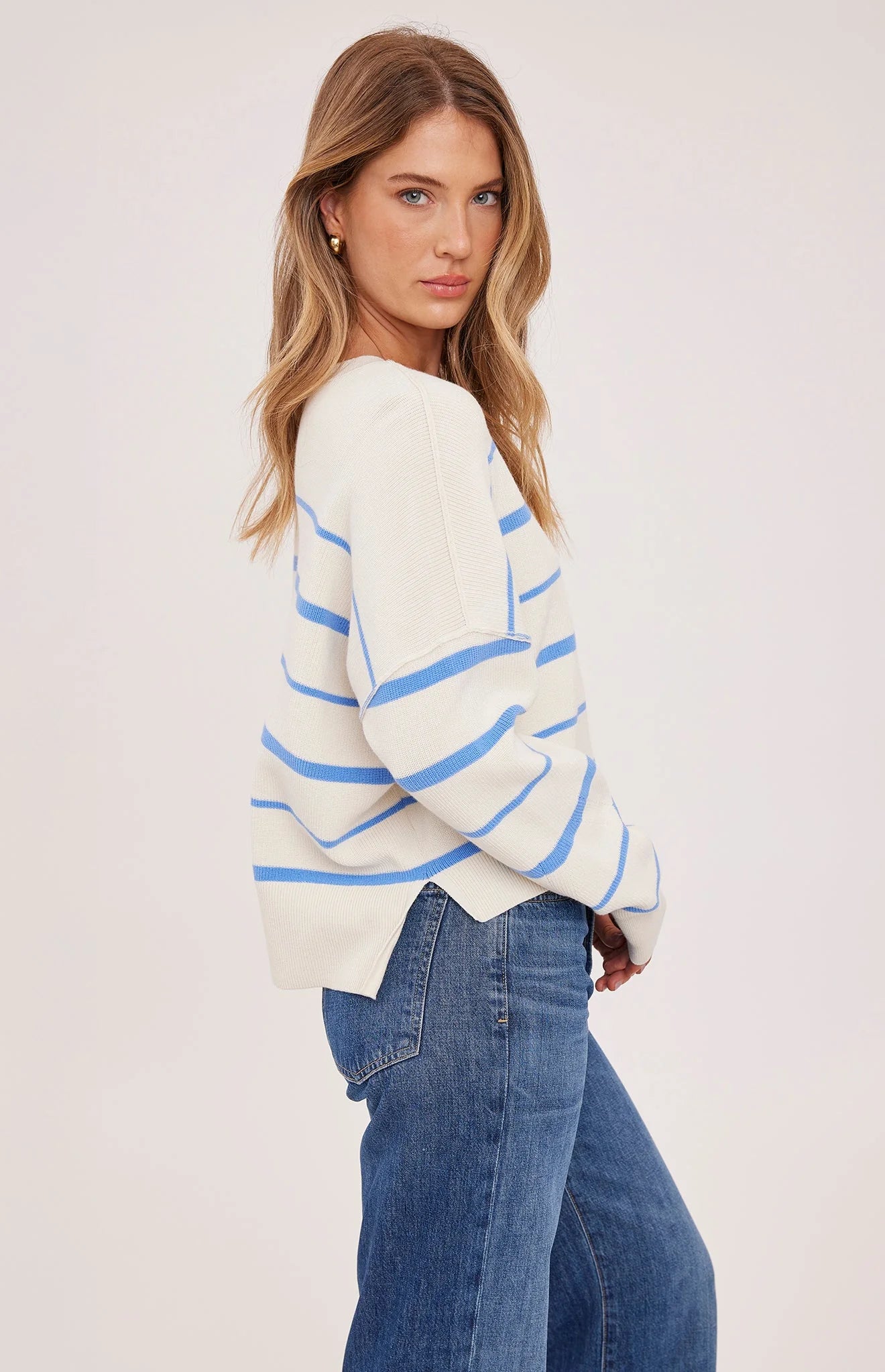 Woman wearing a white sweater with blue stripes and blue jeans on a light background