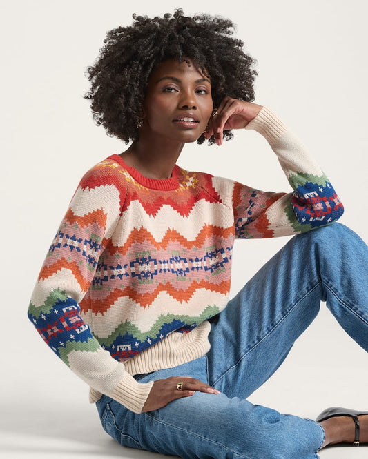 Person wearing a colorful patterned sweater and blue jeans sitting on a white background