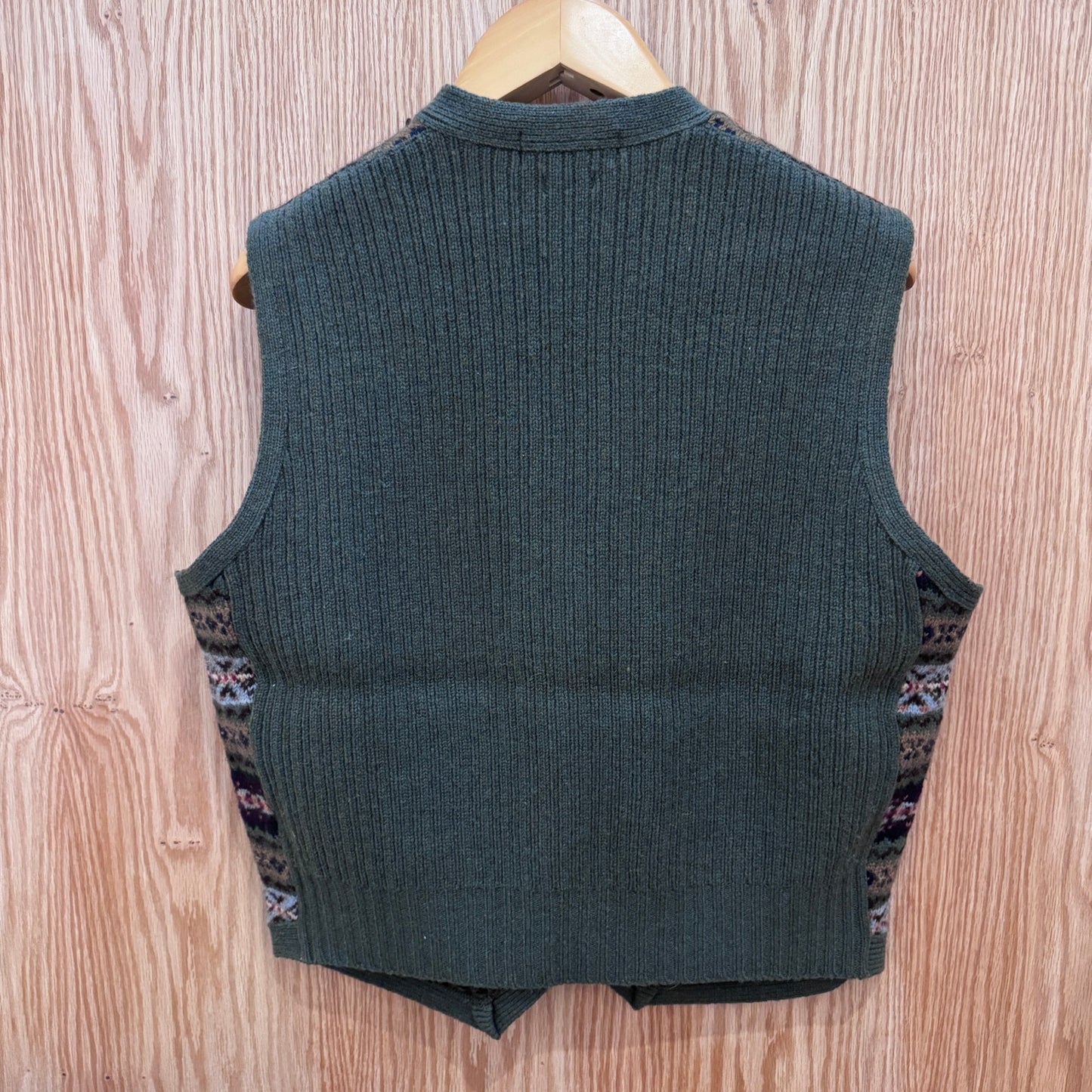 Green ribbed knit vest on a wooden hanger against a wooden background