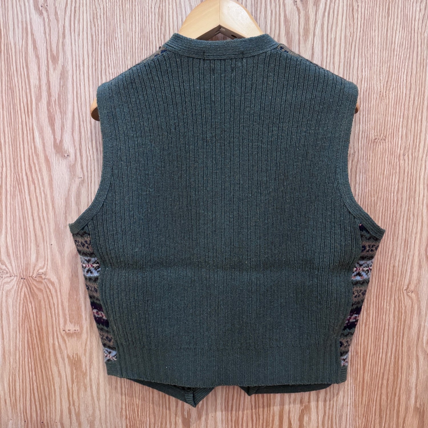 Green ribbed knit vest on a wooden hanger against a wooden background