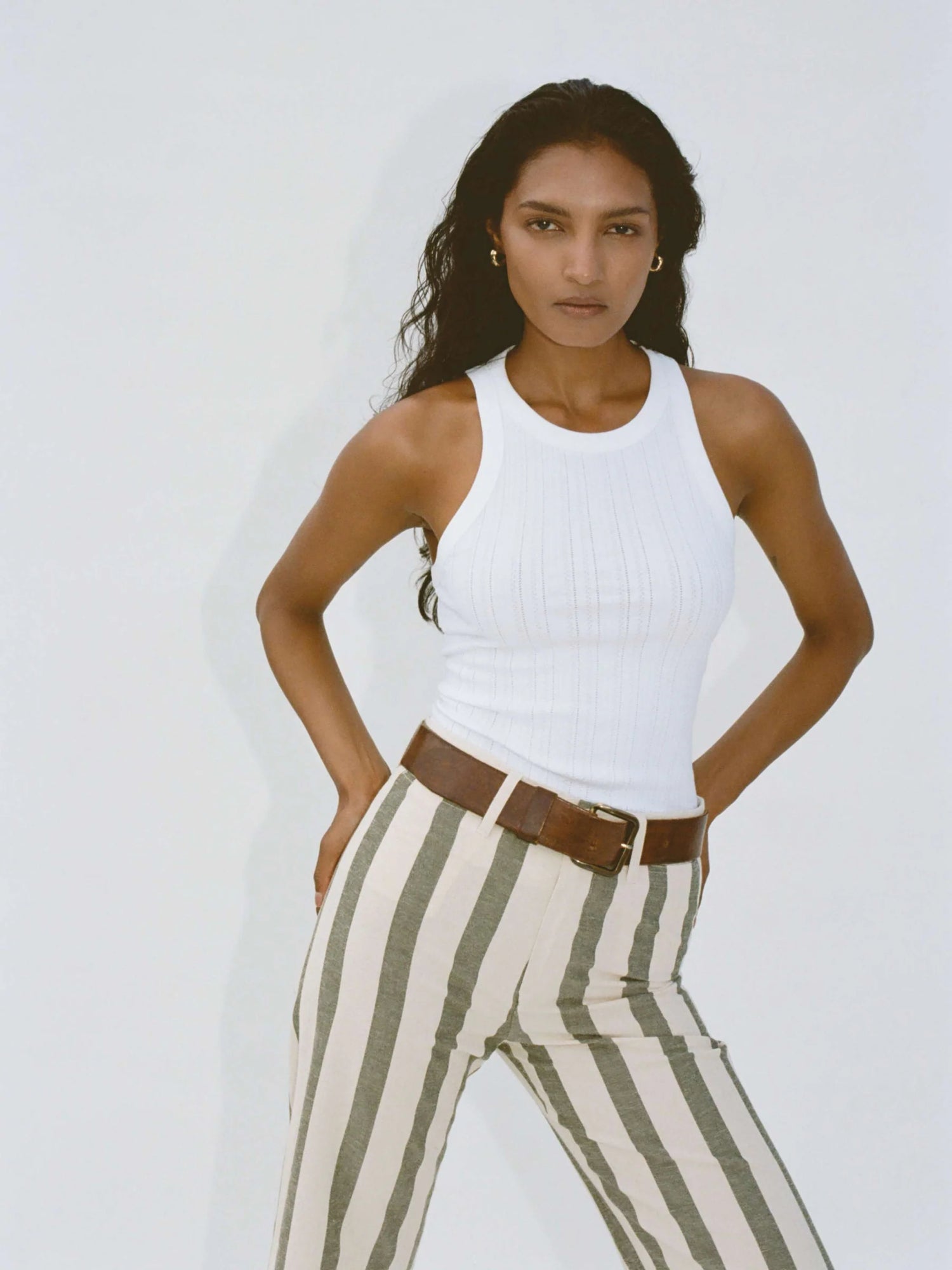 Woman wearing a white tank top and striped pants against a plain background