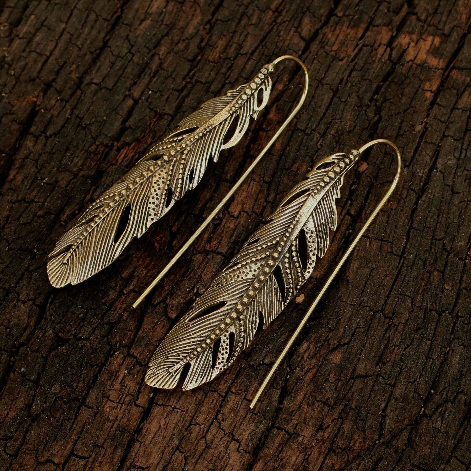 Feather-shaped earrings on a textured wooden surface