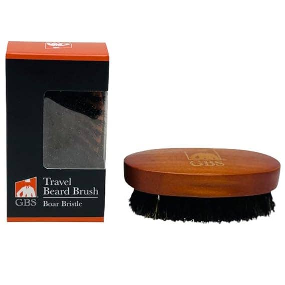 Travel beard brush with GBS branding next to its packaging on a white background