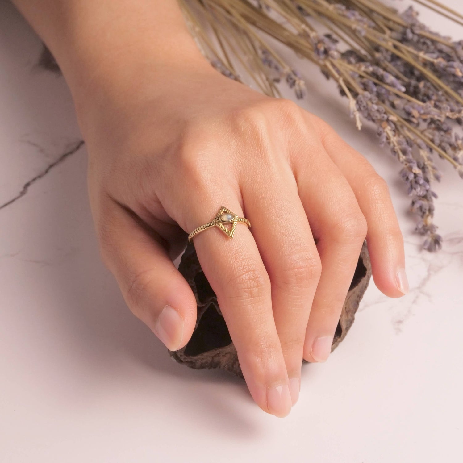 Hand wearing a gold ring with dried lavender flowers on a marble surface