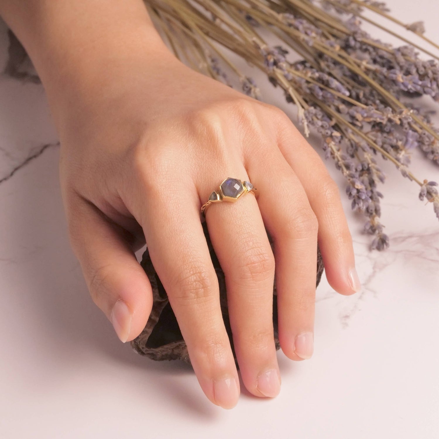 Hand wearing a ring with a purple gemstone against a soft background
