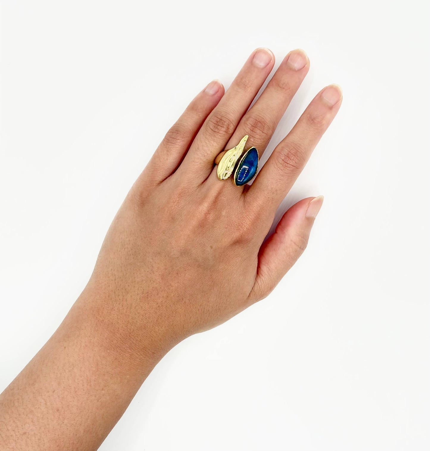 Hand wearing a ring with a blue stone and gold accent on a white background