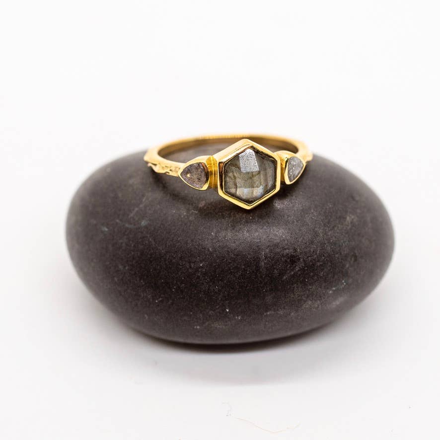 Gold ring with a hexagonal gemstone on a dark stone surface