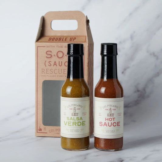 Two hot sauce bottles with labels and a cardboard packaging box on a marble surface.