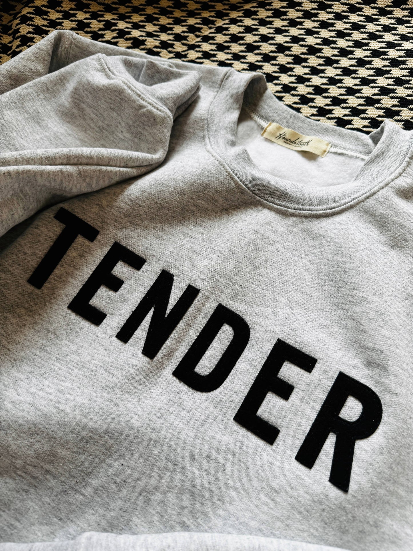 Gray sweatshirt with 'TENDER' text on a checkered floor background